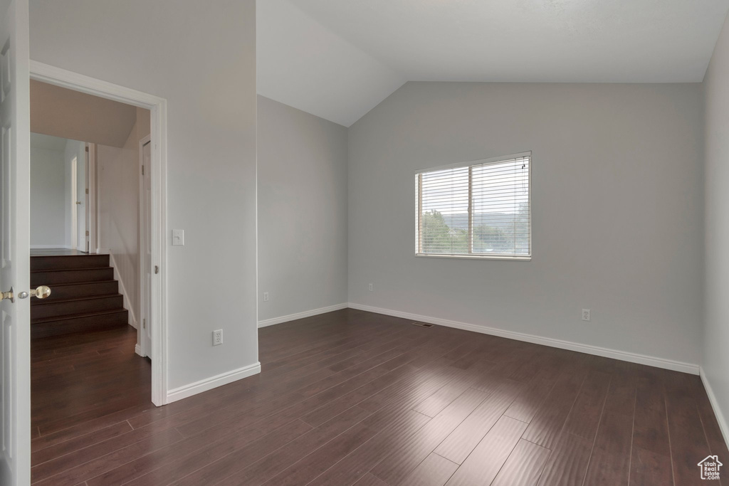 Spare room featuring baseboards, dark wood finished floors, lofted ceiling, and stairway