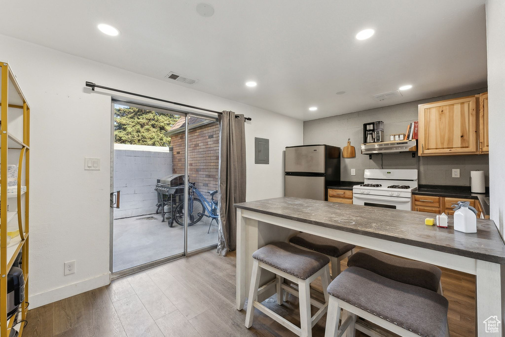 Kitchen featuring white gas range, freestanding refrigerator, dark countertops, under cabinet range hood, and light wood-style flooring