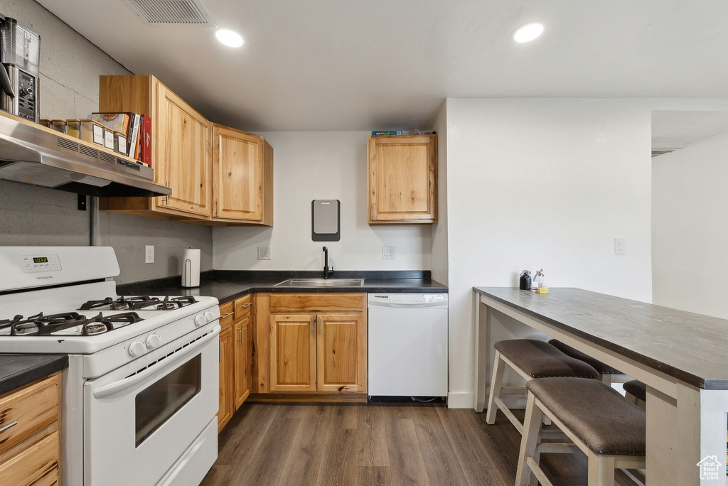 Kitchen with white appliances, a sink, dark wood finished floors, dark countertops, and recessed lighting