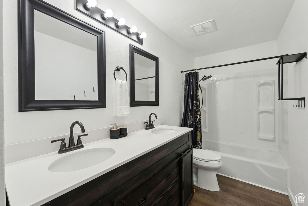Bathroom with wood finished floors, toilet, shower / tub combo with curtain, and double vanity
