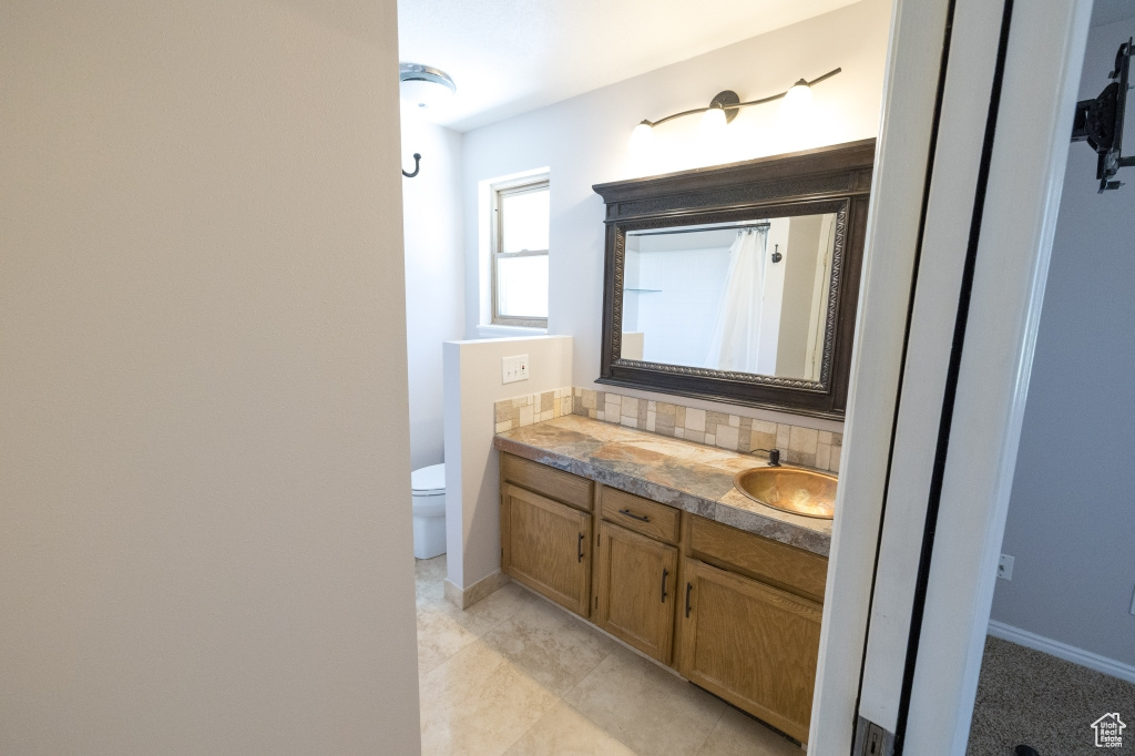 Full bath with vanity, toilet, decorative backsplash, baseboards, and a shower with curtain