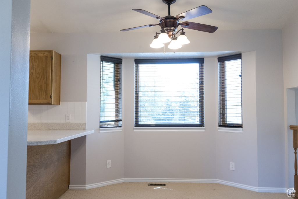 Unfurnished dining area with ceiling fan, baseboards, and light carpet