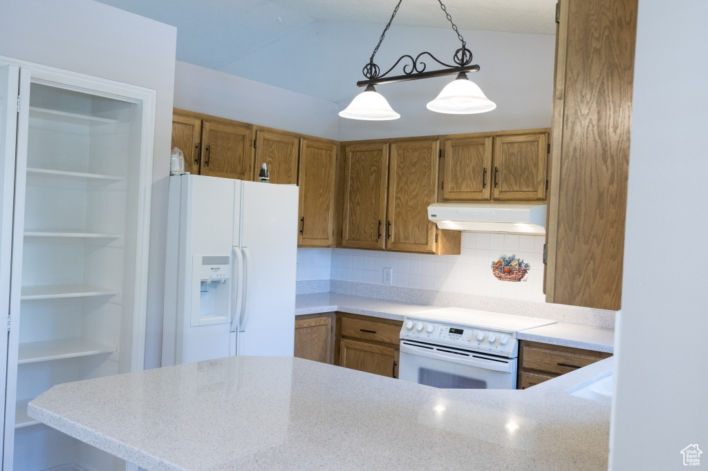 Kitchen with under cabinet range hood, white appliances, brown cabinetry, hanging light fixtures, and light countertops