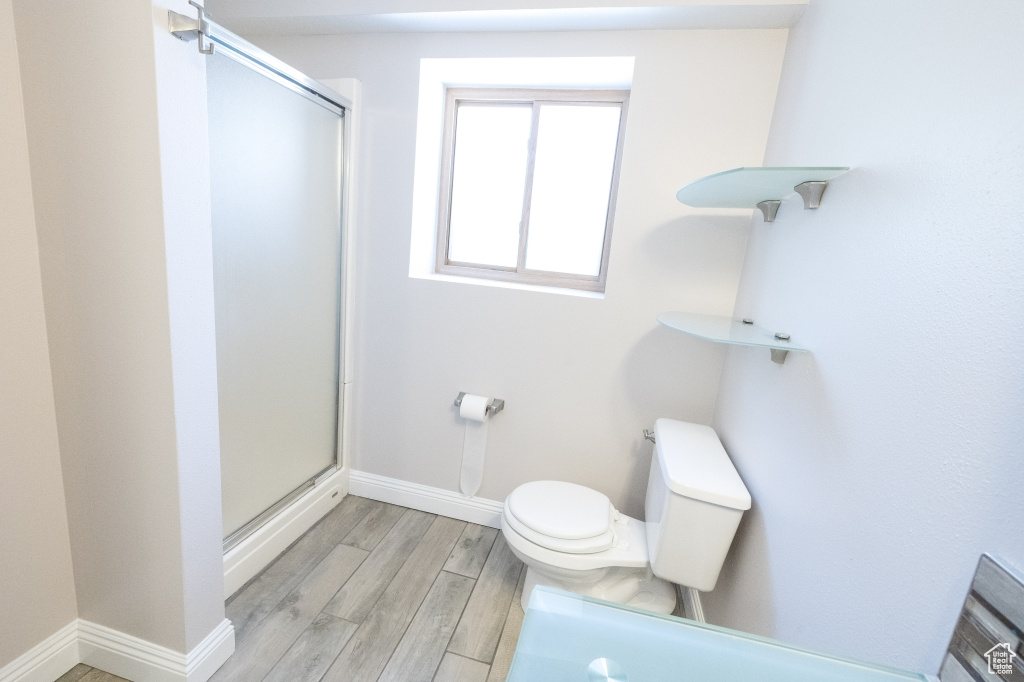 Full bathroom with a stall shower, toilet, wood finished floors, and baseboards