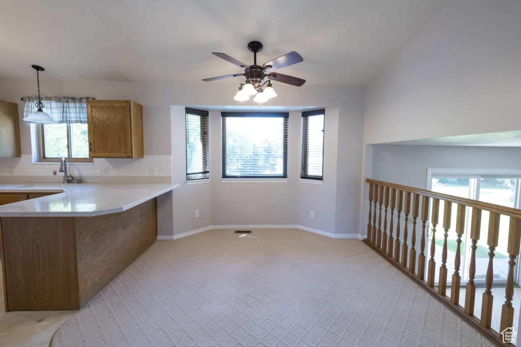 Kitchen featuring brown cabinetry, light countertops, light colored carpet, ceiling fan, and a peninsula