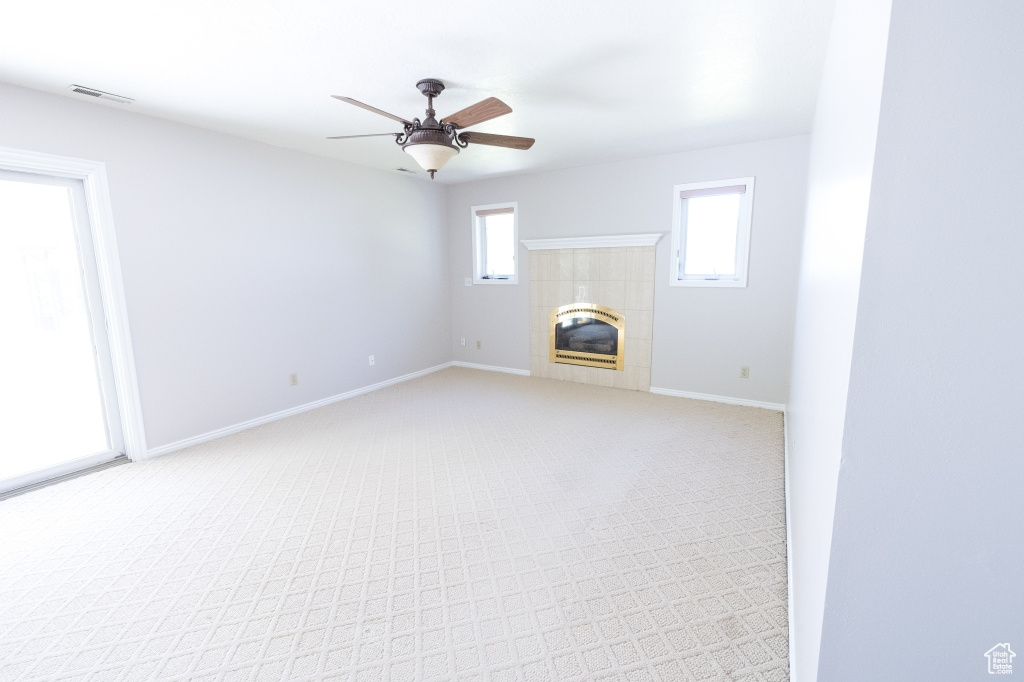 Unfurnished living room with light carpet, a ceiling fan, a fireplace, and baseboards