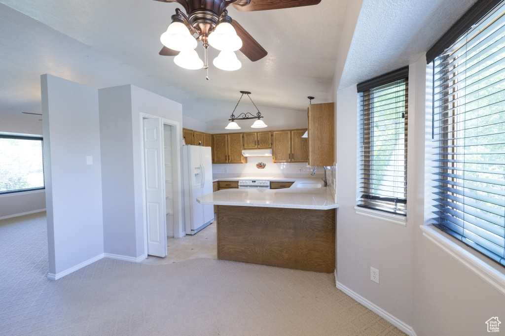 Kitchen with white appliances, under cabinet range hood, light countertops, brown cabinets, and light carpet