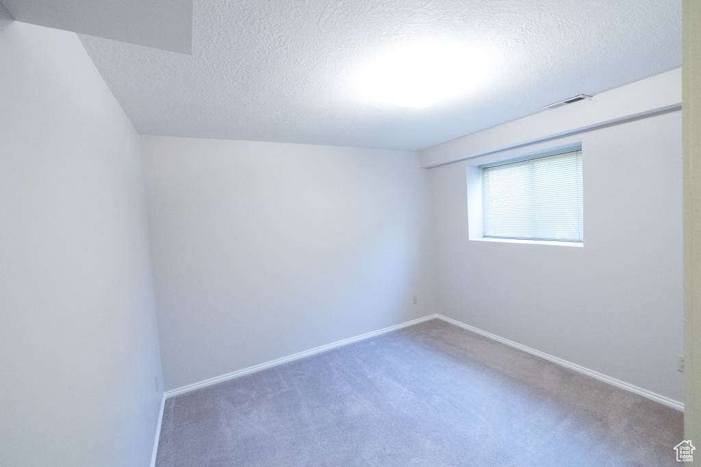 Carpeted empty room featuring a textured ceiling and baseboards