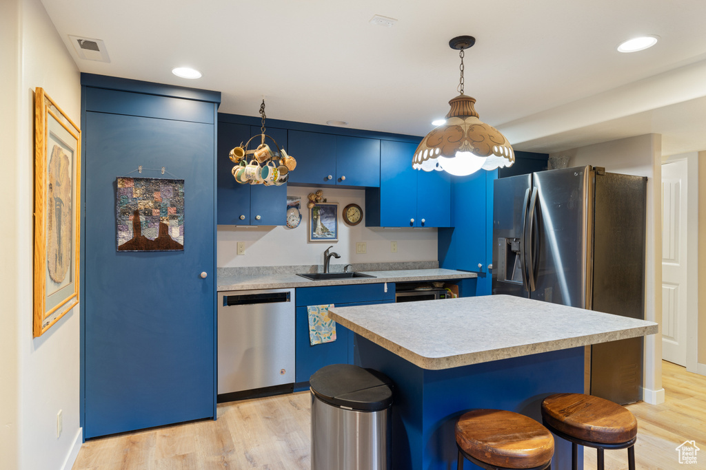 Kitchen featuring appliances with stainless steel finishes, blue cabinetry, a sink, light countertops, and a kitchen breakfast bar