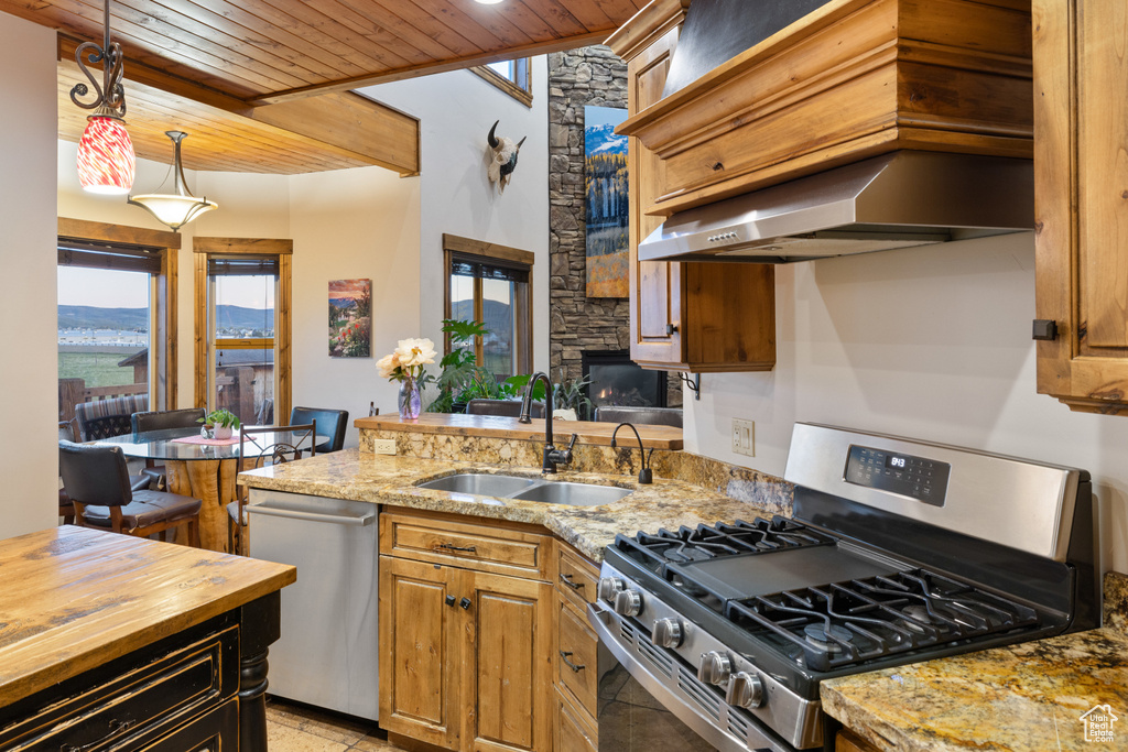 Kitchen with appliances with stainless steel finishes, a sink, wooden ceiling, light stone countertops, and pendant lighting