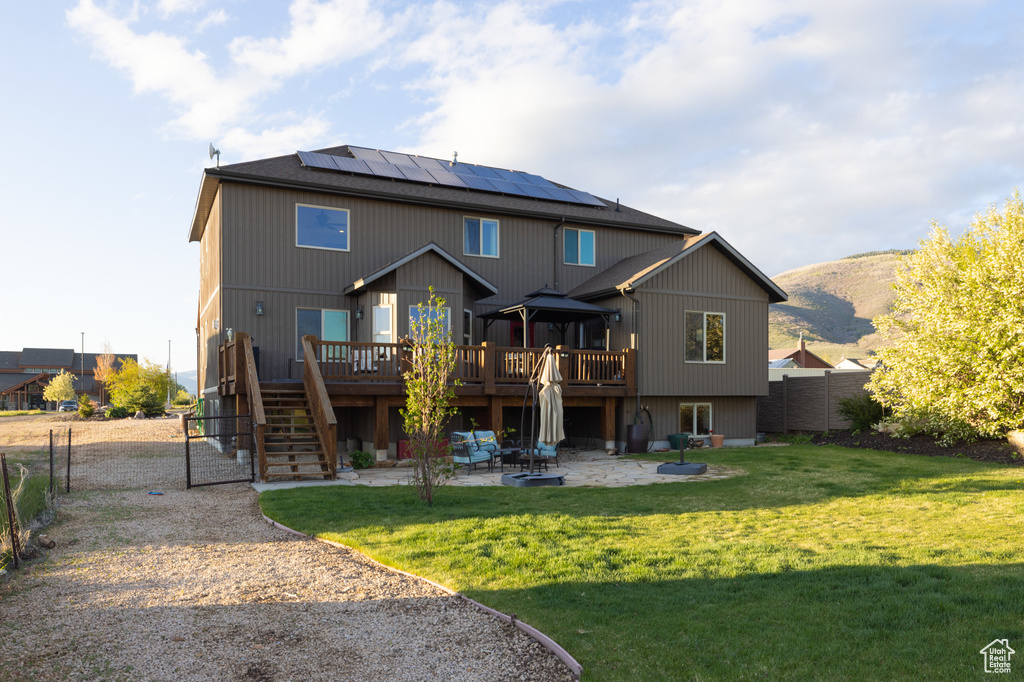 Rear view of property featuring a patio, a deck with mountain view, solar panels, stairs, and a gate
