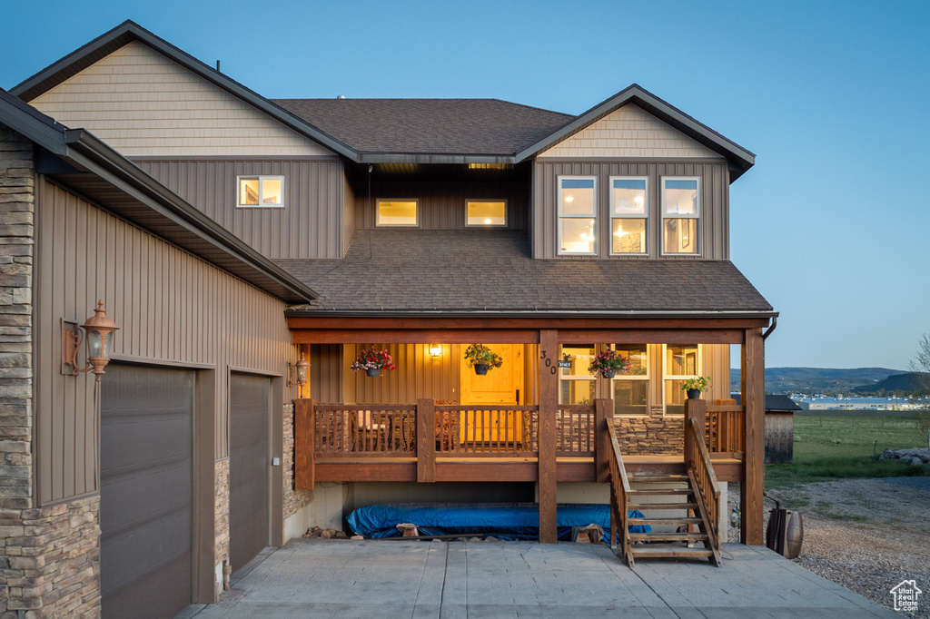 View of front facade with covered porch, a shingled roof, a garage, and driveway