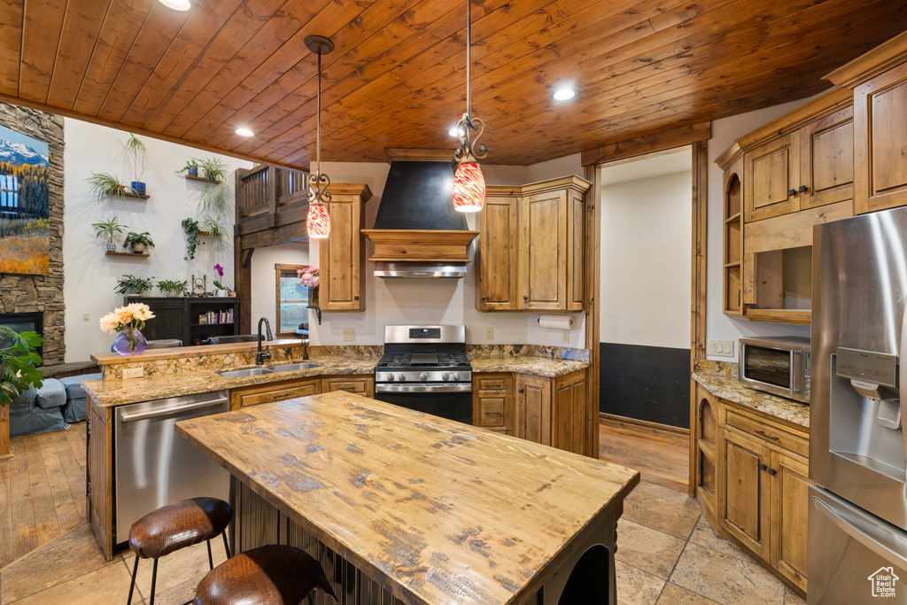 Kitchen featuring appliances with stainless steel finishes, a sink, wood ceiling, custom exhaust hood, and a peninsula