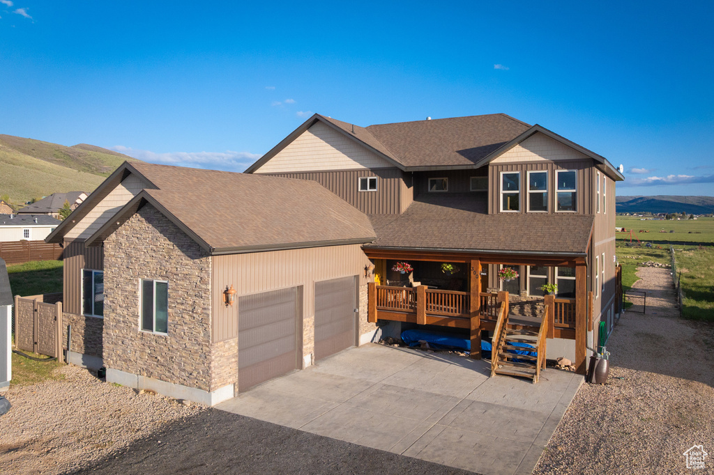 View of front of home with stone siding, an attached garage, roof with shingles, driveway, and a mountain view