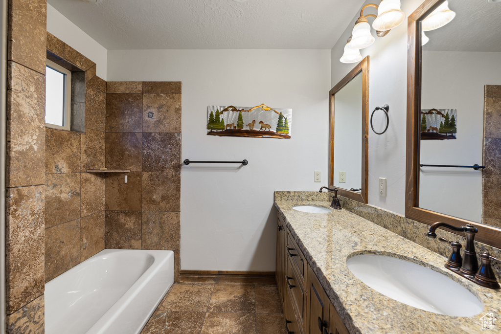 Full bath with double vanity, baseboards, bathtub / shower combination, and stone tile floors