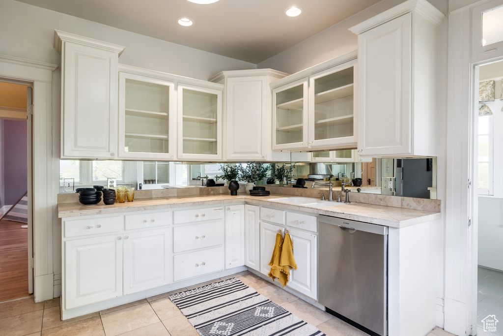 Kitchen with dishwasher, a sink, light countertops, white cabinetry, and glass insert cabinets