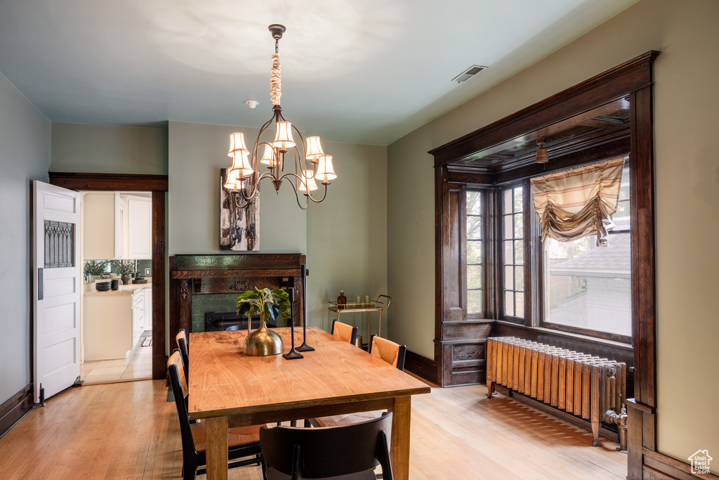 Dining room with radiator heating unit, light wood-type flooring, a chandelier, a fireplace, and baseboards