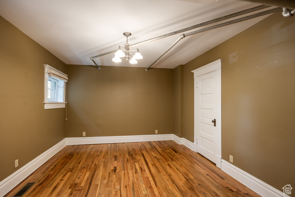 Unfurnished room with a chandelier, wood finished floors, and baseboards