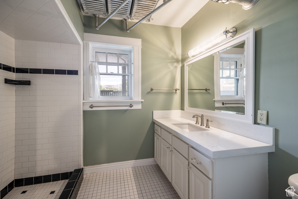 Bathroom featuring a tile shower, vanity, healthy amount of natural light, and toilet