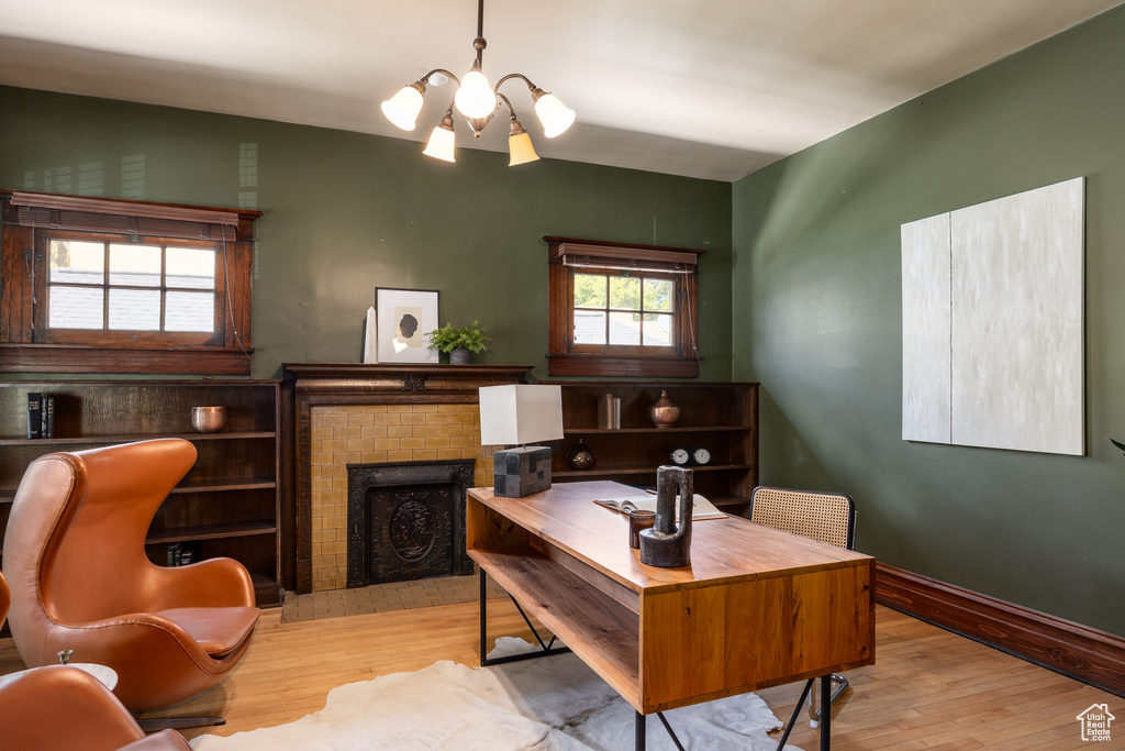 Home office featuring wood finished floors, a chandelier, a brick fireplace, and baseboards