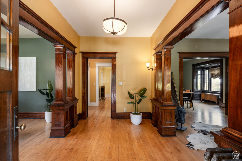 Entryway featuring decorative columns, radiator heating unit, light wood finished floors, and baseboards
