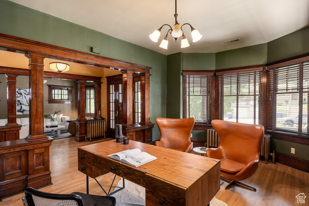 Home office featuring a chandelier, light wood-style flooring, ornate columns, and baseboards