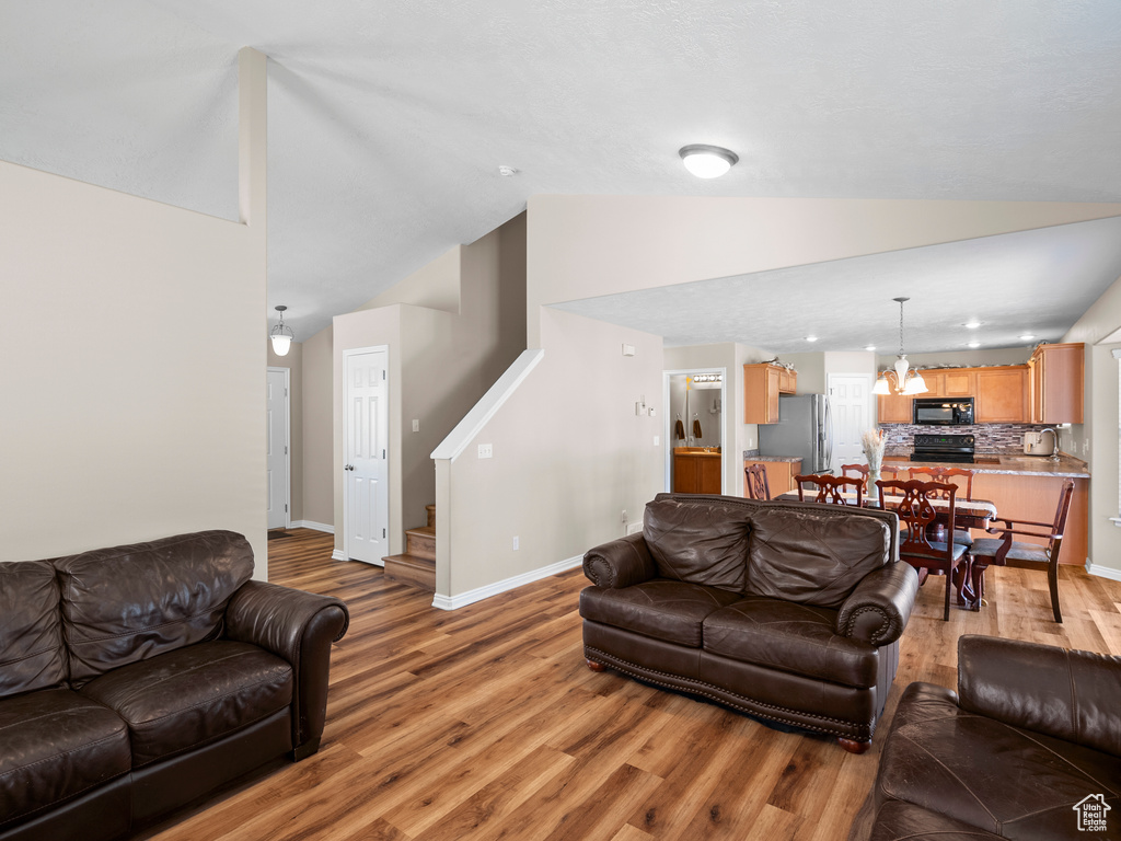 Living area with lofted ceiling, light wood-style flooring, baseboards, and stairs