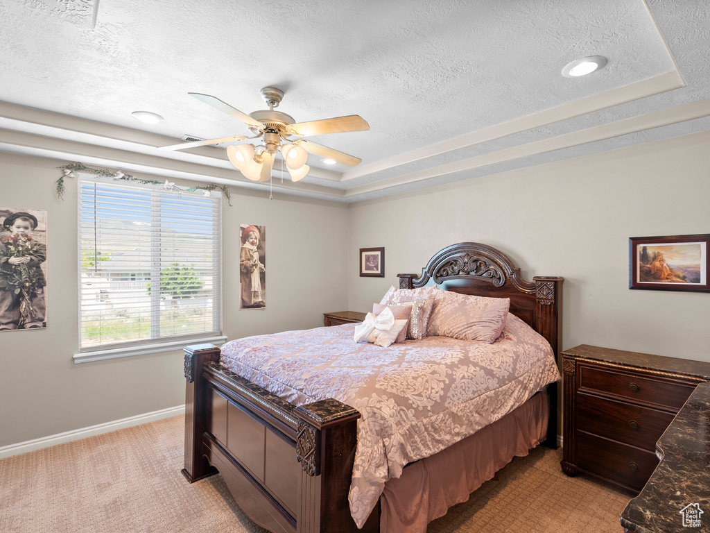 Bedroom with a textured ceiling, a raised ceiling, light carpet, baseboards, and ceiling fan