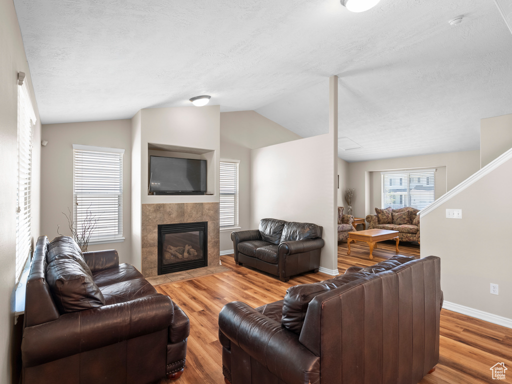 Living room with wood finished floors, lofted ceiling, baseboards, a tiled fireplace, and a textured ceiling
