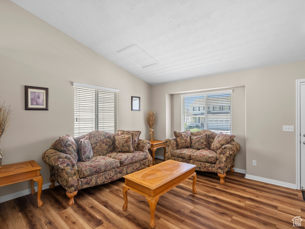 Living room with lofted ceiling, wood finished floors, baseboards, and attic access