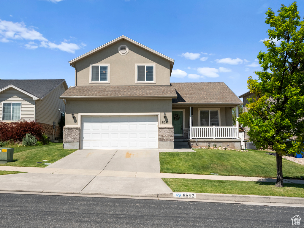 Traditional-style home featuring a porch, a front yard, concrete driveway, and stucco siding
