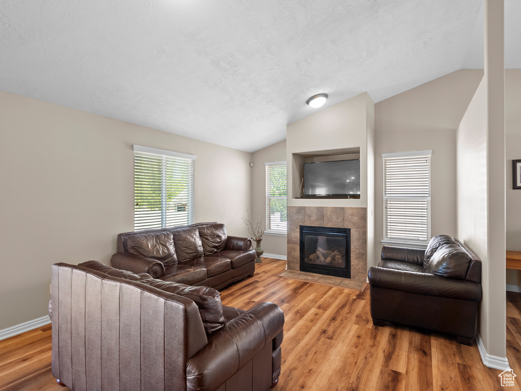 Living room featuring vaulted ceiling, a tile fireplace, light wood-type flooring, baseboards, and a textured ceiling