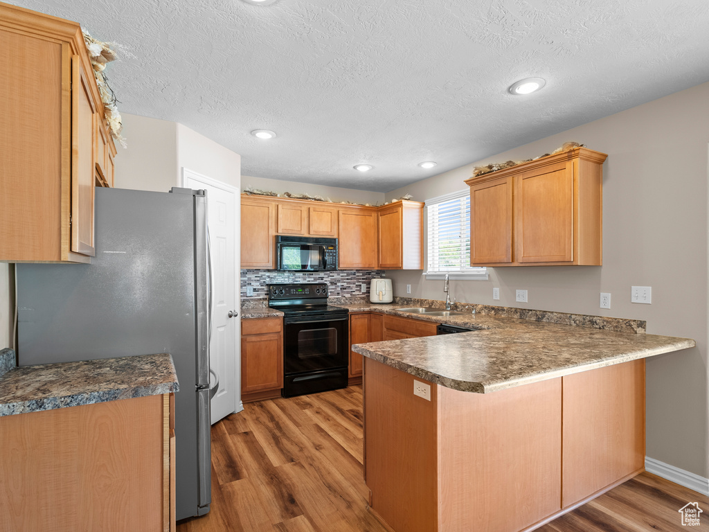 Kitchen with black appliances, a peninsula, a sink, light wood-type flooring, and a textured ceiling