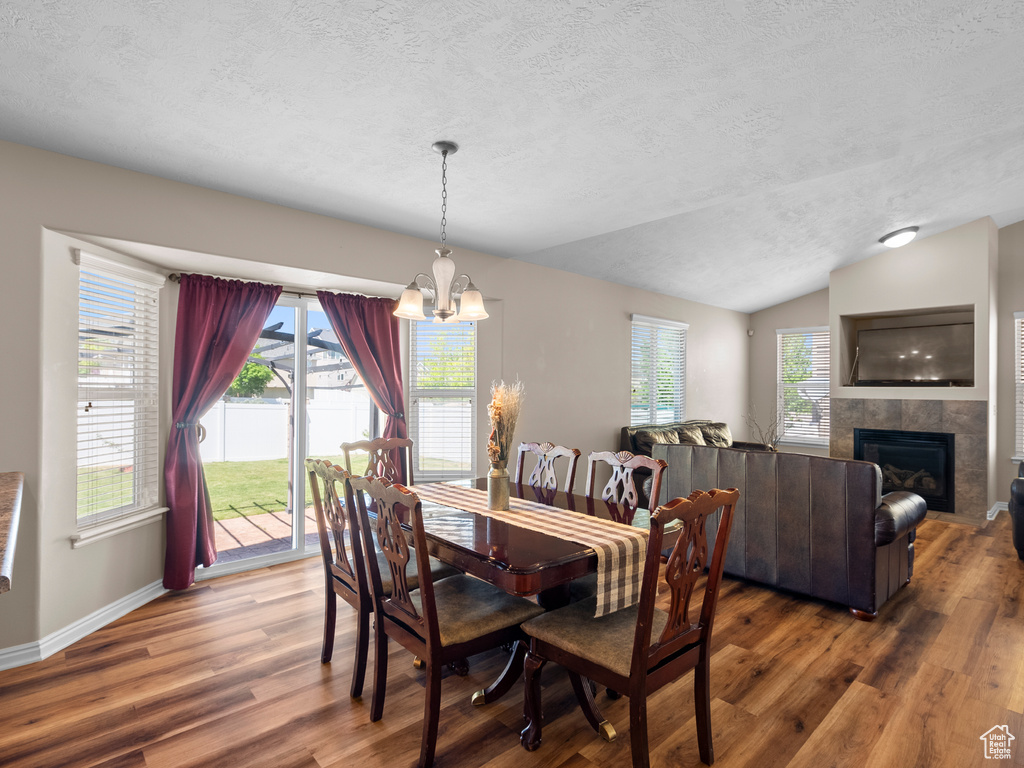 Dining area featuring a textured ceiling, wood finished floors, a chandelier, vaulted ceiling, and a tiled fireplace
