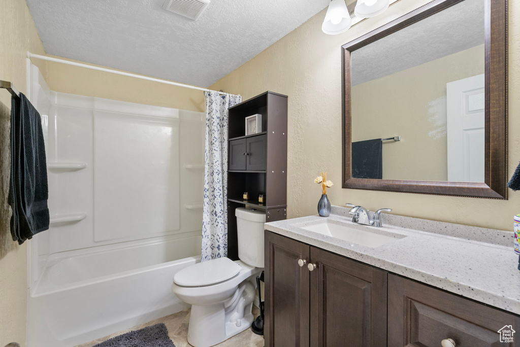 Full bath with a textured ceiling, vanity, toilet, shower / bathtub combination with curtain, and a textured wall