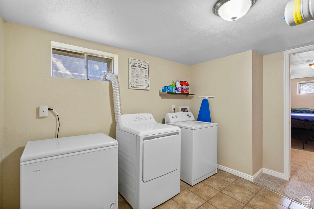 Laundry room featuring separate washer and dryer, baseboards, light tile patterned floors, and a textured ceiling