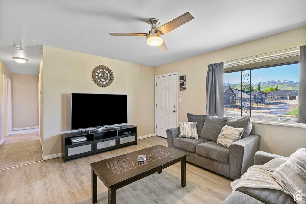 Living room with a ceiling fan, light wood finished floors, and baseboards