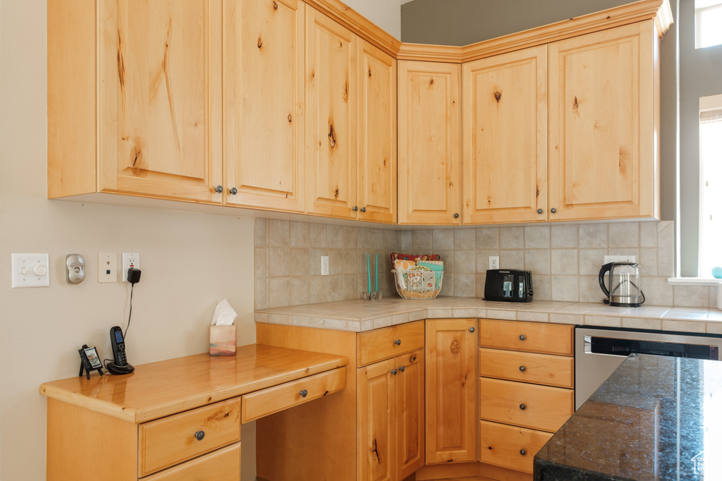 Kitchen with decorative backsplash, light brown cabinets, and stainless steel dishwasher
