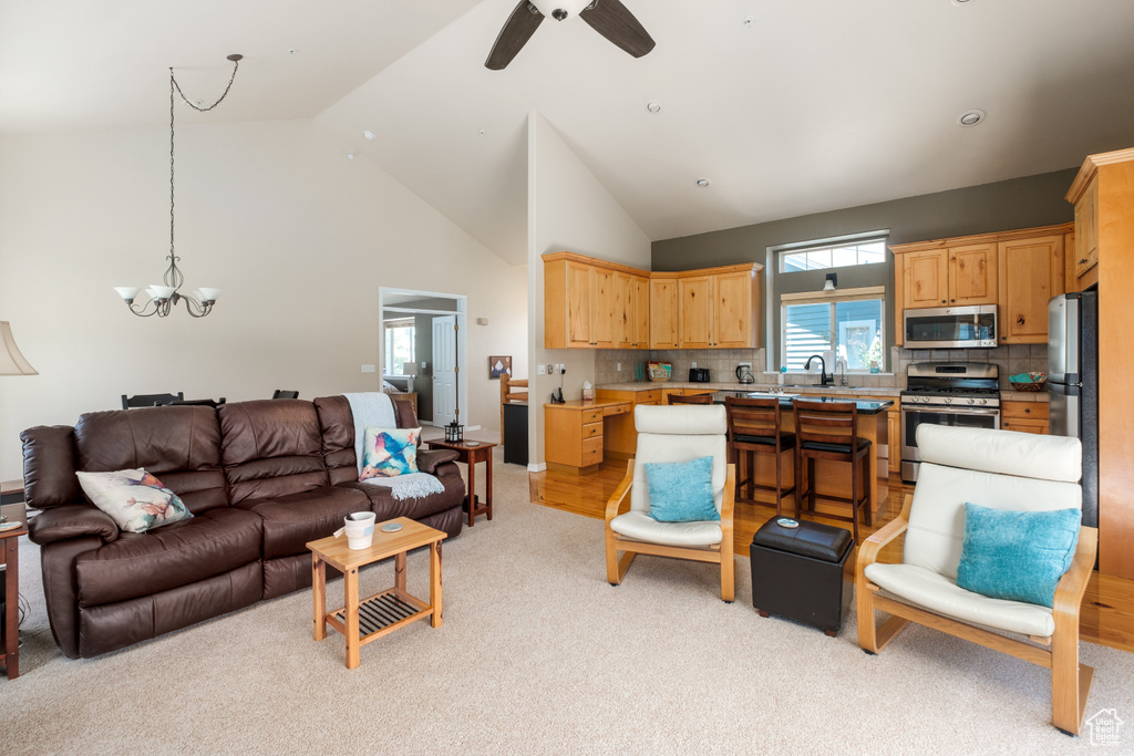 Living room featuring light carpet, a chandelier, high vaulted ceiling, and a ceiling fan