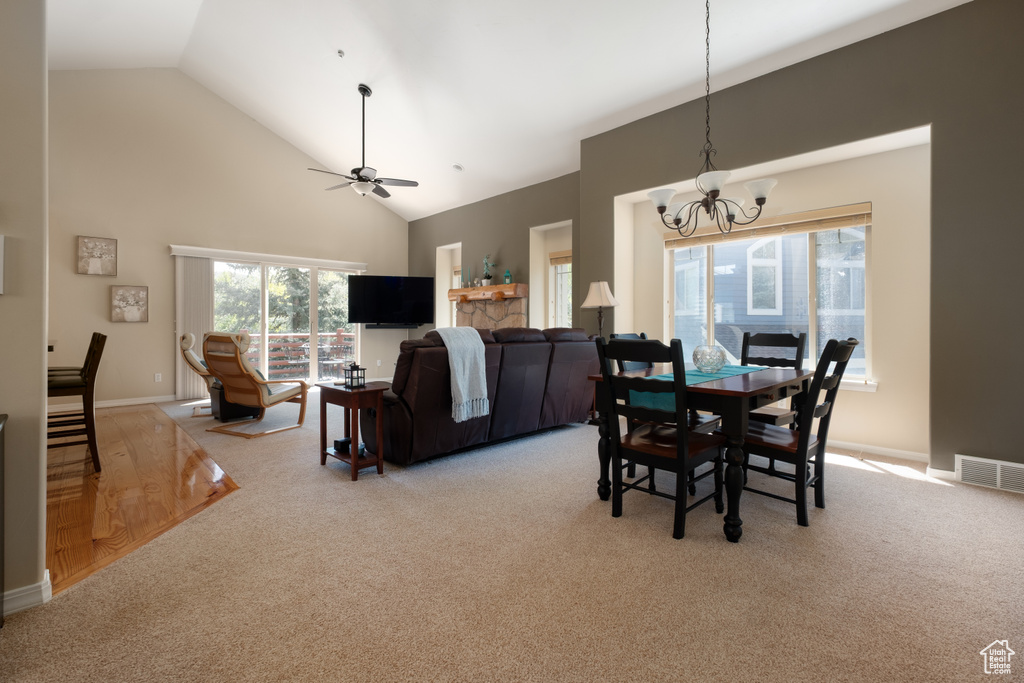 Dining room with high vaulted ceiling, light colored carpet, a chandelier, a ceiling fan, and baseboards