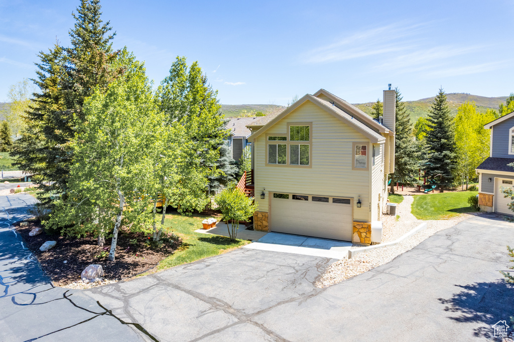 Traditional-style house with driveway, a garage, stone siding, a chimney, and a front lawn