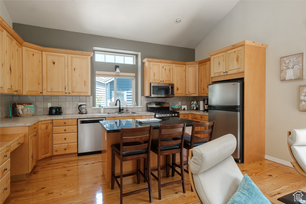 Kitchen featuring appliances with stainless steel finishes, light brown cabinets, a sink, a breakfast bar area, and vaulted ceiling
