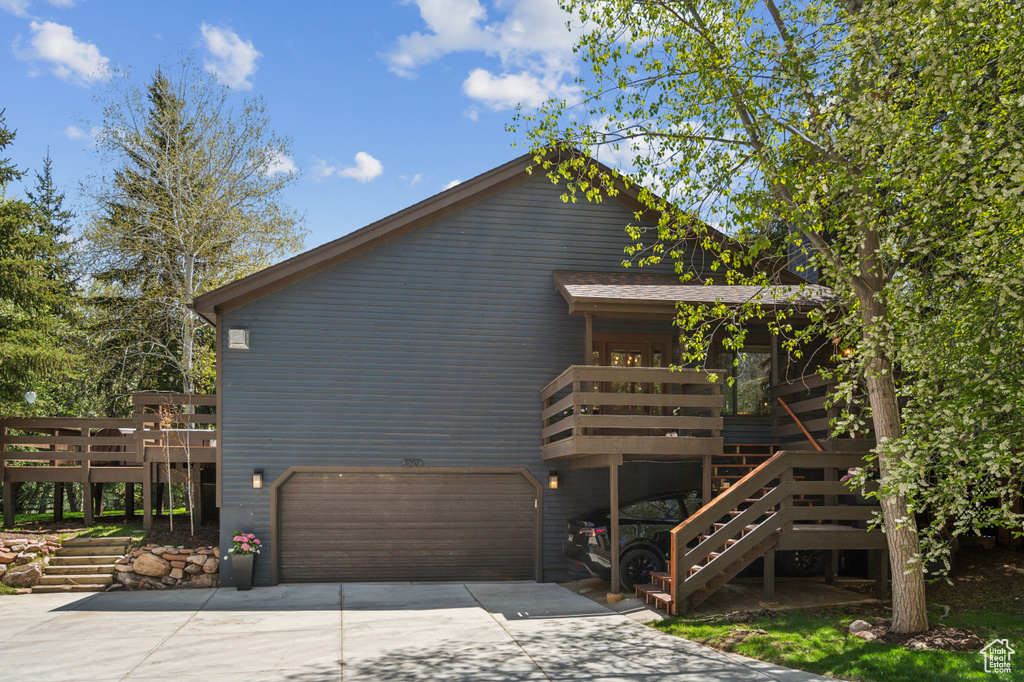 View of side of home featuring concrete driveway, a deck, an attached garage, and stairway