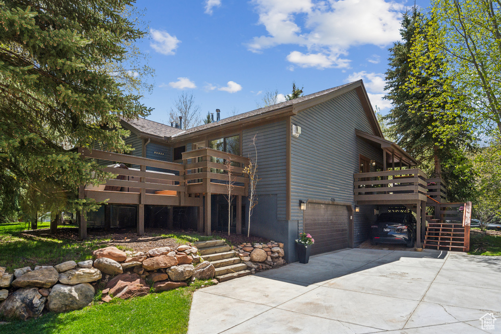 View of front facade with concrete driveway, a deck, an attached garage, a carport, and stairs