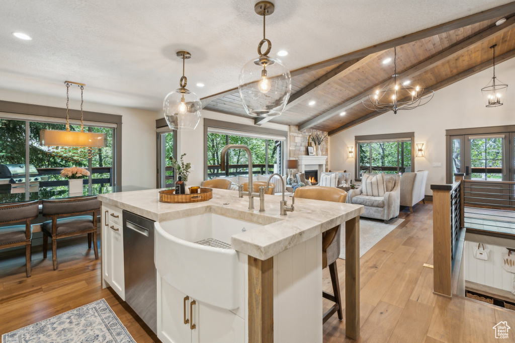 Kitchen with white cabinetry, a large fireplace, stainless steel dishwasher, a sink, and light wood finished floors