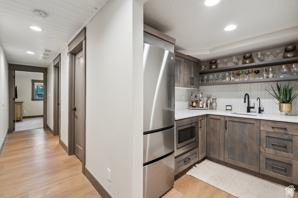 Indoor wet bar with stainless steel appliances, tasteful backsplash, light wood-style flooring, recessed lighting, and baseboards