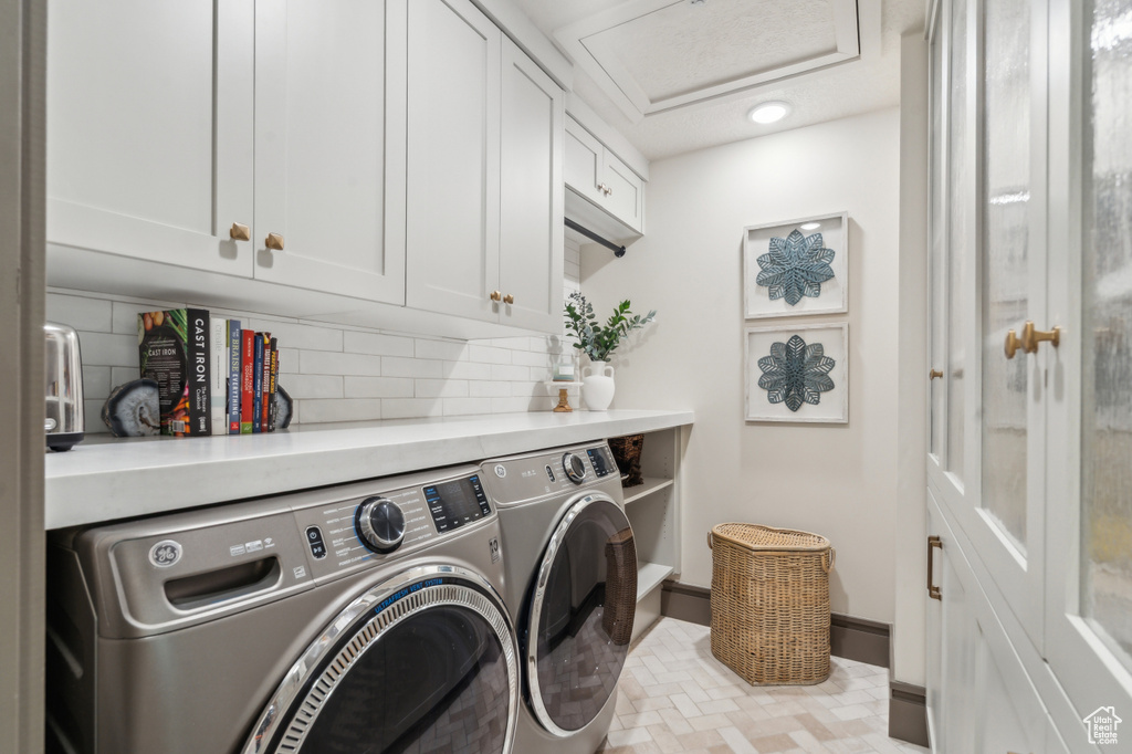 Laundry room featuring cabinet space, washer and clothes dryer, attic access, brick patterned floors, and baseboards