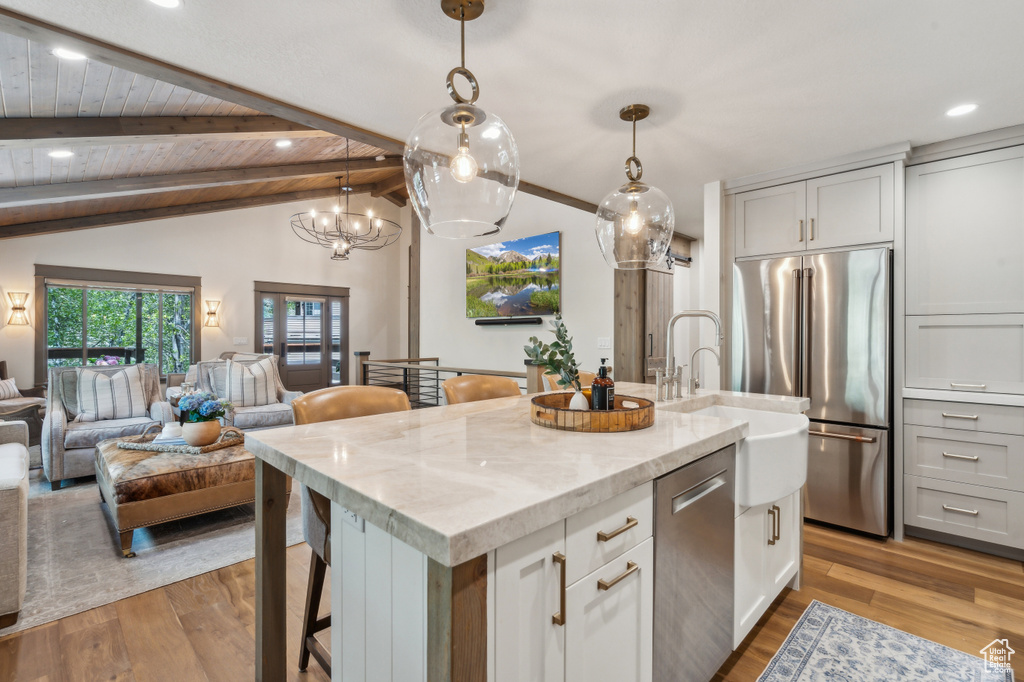 Kitchen featuring appliances with stainless steel finishes, an island with sink, light wood-style flooring, open floor plan, and light stone counters