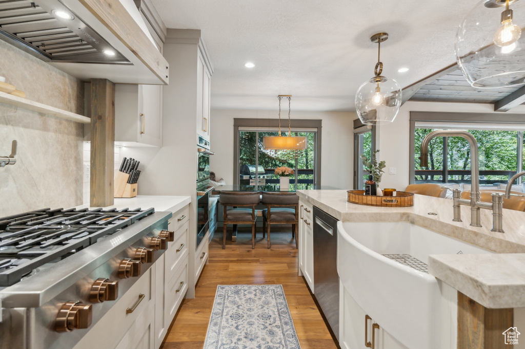 Kitchen featuring a sink, appliances with stainless steel finishes, premium range hood, decorative light fixtures, and light wood-type flooring