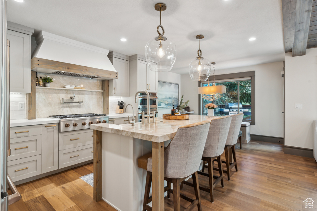 Kitchen featuring stainless steel appliances, custom exhaust hood, decorative backsplash, recessed lighting, and light wood-type flooring